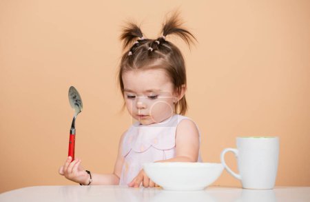 Photo for Baby food, babies eating. Portrait of cute Caucasian child kid with spoon. Hungry messy baby with plate after eating puree - Royalty Free Image