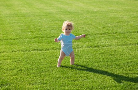 Téléchargez les photos : Bébé debout pieds nus sur la pelouse verte. Enfant en bonne santé - en image libre de droit