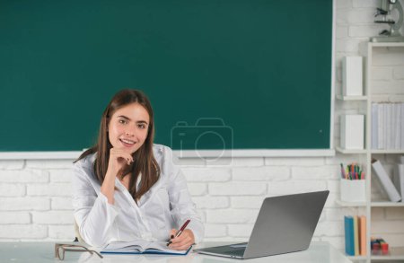 Téléchargez les photos : Portrait d'un jeune collégien souriant étudiant en classe. Femme pigiste ou étudiante avec ordinateur portable - en image libre de droit