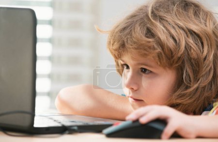 Téléchargez les photos : Gros plan portrait de l'écolier regardant l'ordinateur portable pendant la leçon. Éducation et apprentissage pour les enfants - en image libre de droit