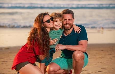 Foto de Joven abrazo familiar en la playa. Familia abrazándose con su hijo, de pie en la playa de verano junto al mar - Imagen libre de derechos