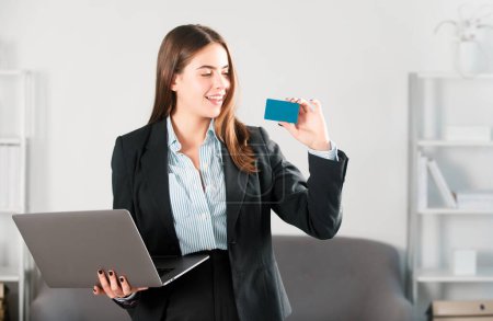 Téléchargez les photos : Portrait d'une femme d'affaires tenant un ordinateur portable et une carte de crédit à l'intérieur du bureau. Services financiers, concept bancaire par carte de crédit - en image libre de droit
