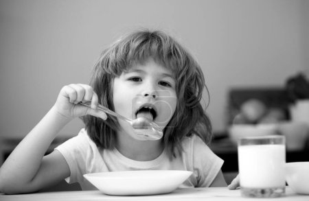 Photo for Portrait of cute child eating soup meal or breakfast having lunch by the table at home with spoon. Kids healthy food - Royalty Free Image