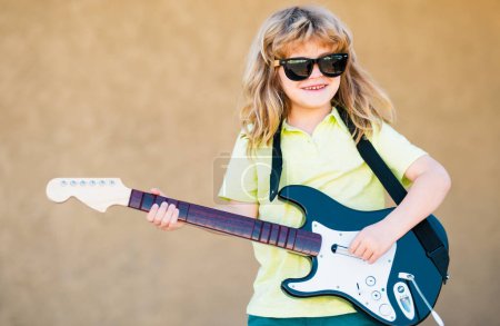 Foto de Boy with guitar. Child plays a guitar and sings, kids music and song. Funny little hipster musician child playing guitar - Imagen libre de derechos