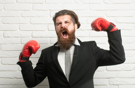 Téléchargez les photos : Un fou de boxe. Homme d'affaires boxeur excité drôle. Jeune homme en costume et gants de boxe, gagnant. Furieux drôle barbu homme d'affaires - en image libre de droit