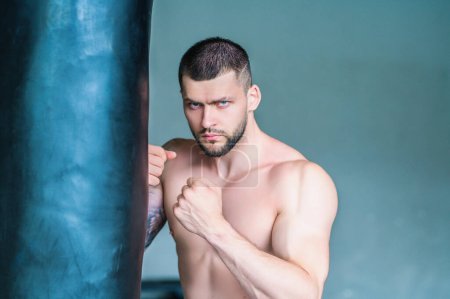 Photo for Strong young man boxer boxing in gym. Sporty male workout with punchbag boxing bag in sports club. Young man has fitness workout. Hard boxing. Male athlete does exercise, sport - Royalty Free Image