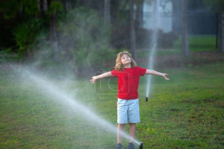 Photo for Garden watering systems. Child play with watering sprinkler system in backyard. Little kid playing with garden watering hose in backyard. Child having fun with spray of water. Watering grass - Royalty Free Image
