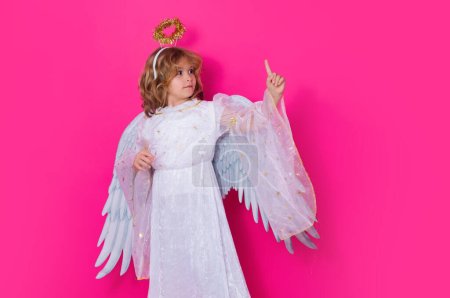 Téléchargez les photos : Petit ange pointant du doigt, geste pointu. Enfant en costume d'ange robe blanche et ailes de plumes. Enfant innocent - en image libre de droit