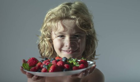 Photo for Close up summer portrait of kid with plate of mix summer fruits. Healthy organic strawberry fruit, summer season - Royalty Free Image