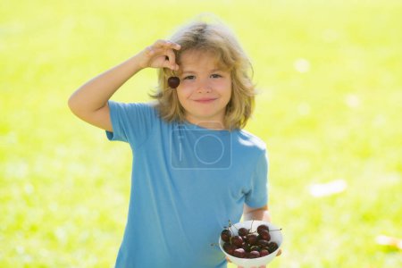 Photo for Summer child face. Happy little child with cherry outdoors. Kid picking and eating ripe cherries in summer park. Child holding fresh fruits. Healthy organic berry cherry fruit, summer season - Royalty Free Image