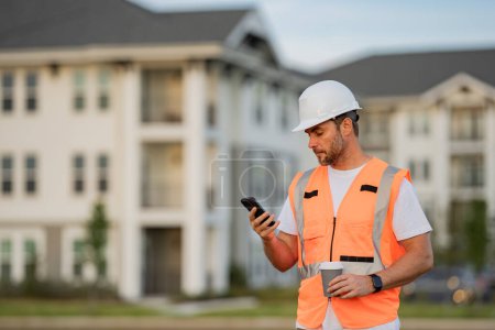 Photo for Engineer builder drinking take away coffee using phone on break. Builder at construction site. Buider with helmet on construction outdoor. Worker at construction site. Bilder in hardhat - Royalty Free Image
