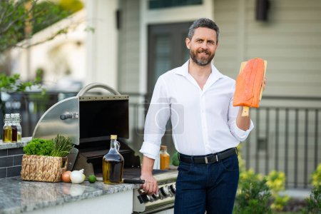 Photo for Handsome man preparing barbecue grill outdoor. Male chef cooking tasty salmon fillet on barbecue grill at backyard. Chef preparing food on barbecue. Millennial man grilling salmon on grill. Bbq party - Royalty Free Image