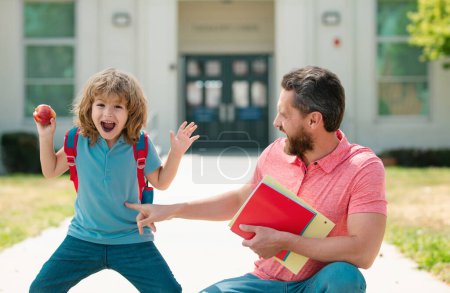 Photo for Parent and amazed pupil of primary school go hand in hand. Teacher in t-shirt and excited schoolboy with backpack taking to school - Royalty Free Image