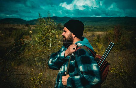 Foto de Caza de montaña. Hunter con escopeta a la caza. Barbudo cazador hombre sosteniendo arma y caminando en el bosque - Imagen libre de derechos