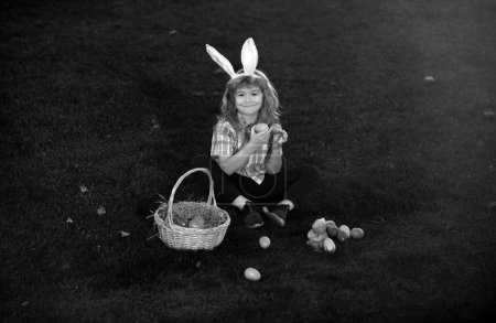 Foto de Conejito con orejas de conejo. Huevos de Pascua en el jardín. Niño jugando en el campo, cazando huevos de Pascua - Imagen libre de derechos