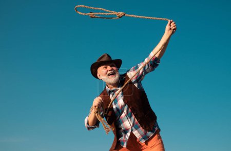 Photo for Old wild west cowboy at rodeo. Western pensioner with lasso rope. Bearded man with brown jacket and hat catching horse or cow - Royalty Free Image