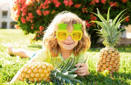 Téléchargez les photos : Enfant portant des lunettes de soleil drôles avec de l'ananas. Enfant aux fruits tropicaux. Des vacances exotiques. Fruits pour enfants. Vacances d'été enfants - en image libre de droit