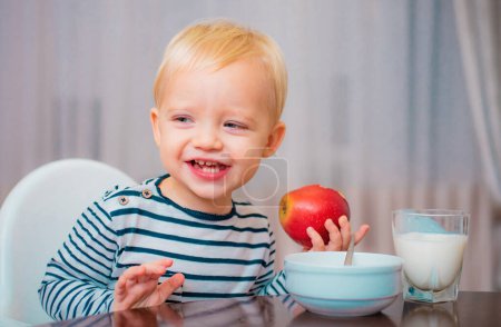 Téléchargez les photos : Enfant mignon garçon assis à la table avec assiette et nourriture. Une nourriture saine. Bébé mignon garçon petit déjeuner. Nutrition pour bébé. Mangez sainement. Un tout-petit qui mange. Une alimentation saine. Concept de vitamine. Enfant manger pomme. - en image libre de droit