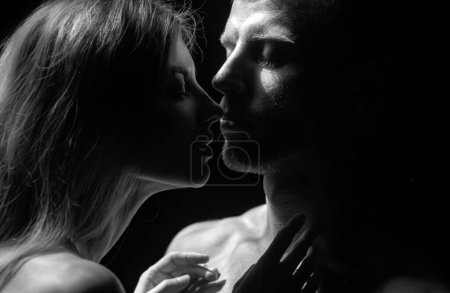 Foto de Un beso sensual. Primer plano retrato del hombre abrazando e ir a besar a la mujer sensual. Pareja cariñosa besándose sobre fondo negro. Amor verdadero en el día de San Valentín - Imagen libre de derechos