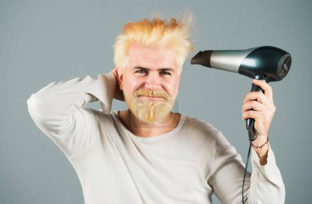Téléchargez les photos : Blond barbu cheveux secs. Beau homme aux cheveux longs sèche ses cheveux avec un sèche-cheveux - en image libre de droit