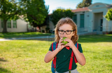 Téléchargez les photos : Enfant avec des sacs à dos dans le parc scolaire. Pupilles avec sacs à dos à l'extérieur. écolier manger pomme - en image libre de droit