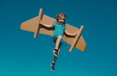 Téléchargez les photos : Joyeux enfant sautant et jouant avec des ailes de jouet sur fond de ciel d'été. Succès des enfants, concept de leader et gagnant - en image libre de droit