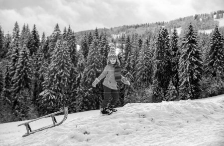 Téléchargez les photos : Drôle de garçon qui s'amuse avec un traîneau dans les forêts d'hiver. Enfants mignons luge dans une montagne de neige. Activités hivernales pour les enfants. Arbres enneigés dans les montagnes sur le paysage hivernal - en image libre de droit