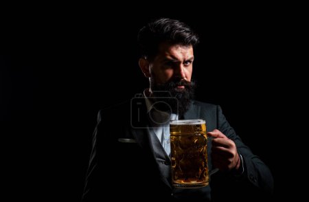 Foto de Serious man in classic suit drinking beer. Bearded guy in business outfit looks happy and satisfied. Portrait of man with lifted high glass of beer on black background - Imagen libre de derechos