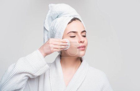 Photo for Closeup of Beautiful Young Woman washing her face with the Cotton Pad on the gray background. Eyes are Closed - Royalty Free Image