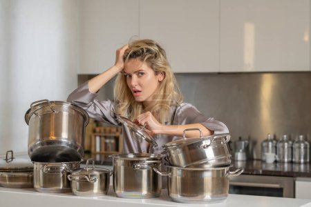 Téléchargez les photos : Femme au foyer ennuyée cuisiner à la cuisine. Style de vie domestique. Une femme fatiguée préparait à manger dans la cuisine le matin. casserole de cuisson - en image libre de droit