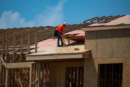 Photo for Roof construction. Roofer on roof structure. Construction Worker on Top of the Wooden House Frame. Worker roofer builder working on roof at construction site. Construction crew working on the roof - Royalty Free Image