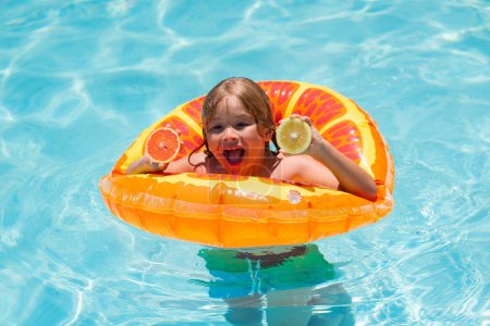 Foto de Niño con naranja en la piscina. Frutas de verano. Lindo niño en la piscina en el día de verano con naranja. Actividad de verano al aire libre para niños. Vacaciones de verano para niños. Niño nadando en la piscina - Imagen libre de derechos