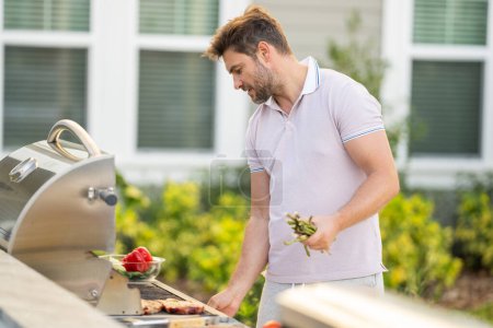 Photo for Men cooking on barbecue grill in yard. Cook at a barbecue grill preparing meat - Royalty Free Image