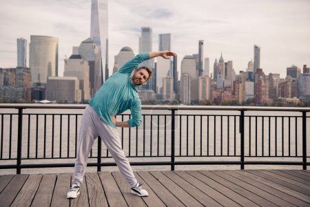 Photo for Senior man in fitness wear workout in NYC. Healthy retirement lifestyle. Active senior man is exercising outdoor. Active after retirement. Mature retired sportsman doing stretching exercises - Royalty Free Image