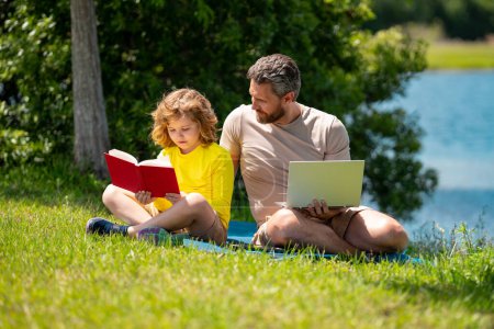Photo for Father with his son reading book together in the summer park. Father and son having a picnic in the park, happiness family concept. Father and son playing at the park at the day time. Friendly family - Royalty Free Image