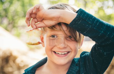 Foto de Niño en unas vacaciones de otoño en la granja. Un niño sonriente sostiene una manzana mordida con una mano. Adiós verano - hola otoño. Venta para toda la colección de otoño, increíbles descuentos y maravillosa opción - Imagen libre de derechos