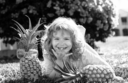 Photo for Boy with pineapple on head, plays with fresh tropical fruit outdoorst. Excited funny kid. Child face with amazed expression. Kids summer party - Royalty Free Image