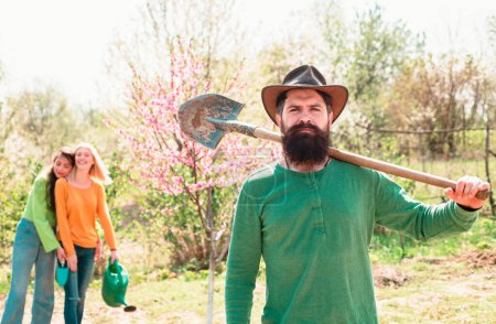 Téléchargez les photos : Homme barbu plantant des plantes dans le jardin de printemps. Le concept de travail d'équipe et d'amitié - en image libre de droit