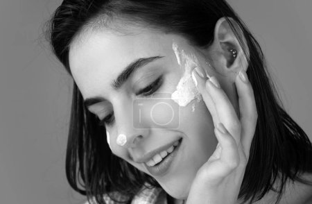 Photo for Beautiful girl model with natural makeup applying moisturizer cream on pretty face - Royalty Free Image