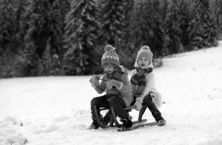 Photo for Kids boy and little girl enjoying a sleigh ride. Children sibling together sledding, play outdoors in snow on mountains in winter. New Year wallpaper, Christmas greeting card - Royalty Free Image