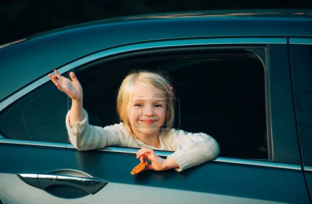 Photo for Cute little girl traveling in the car and observing nature from open window. Little girl waving hand for good bye in the are. Outdoor portrait: beautiful kid smiling and waving say good bye - Royalty Free Image
