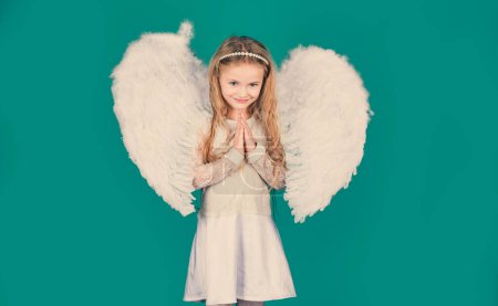 Photo for Valentines Day. Angels little hands crossed for you. Mischievous little angel girl standing with your clenched fists. Beautiful little angel girl standing with your arms close to your chest as in - Royalty Free Image