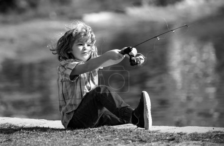 Téléchargez les photos : Pêche d'enfant sur le lac. Petit pêcheur avec fileuse à la rivière. Portrait de garçon excité pêche. Garçon à la jetée avec tige. Concept de pêche - en image libre de droit