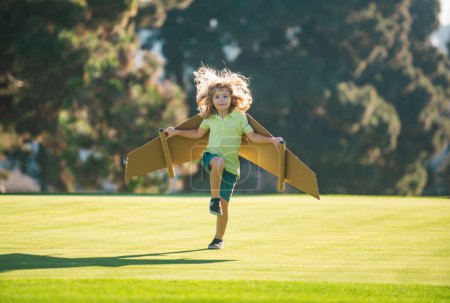 Photo for Kid boy playing with cardboard wings. Child in summer field. Kids travel and vacation concept. Imagination and freedom concept. Boy with wings at field imagines pilot and dreams of flying - Royalty Free Image