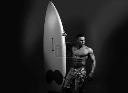 Téléchargez les photos : Serfer bodybuilder tenant la planche de serf. Concept de passe-temps. Athlète masculin avec planche de surf. Musclé corps torse de chaud beau garçon - en image libre de droit