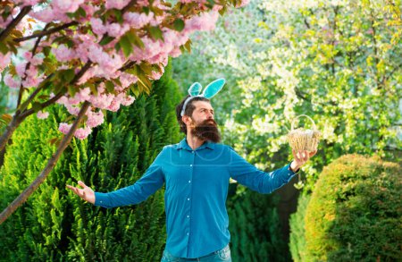 Téléchargez les photos : Concept de chasse aux œufs de Pâques. Série humoristique d'un homme en costume de lapin. Bon pour Pâques ou des situations ironiques. Lapin homme avoir du plaisir dans le parc - en image libre de droit
