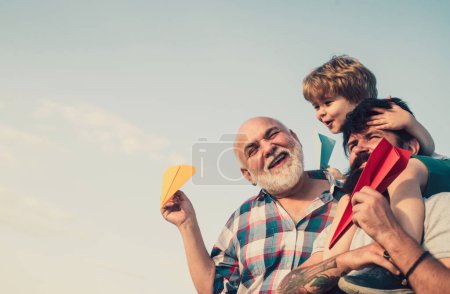 Téléchargez les photos : Génération d'hommes. Joyeux enfant jouant avec jouet avion en papier sur fond de ciel d'été. Mignon fils avec papa jouant en plein air. Bonne famille. Père et fils avec grand-père - heureux famille aimante - en image libre de droit