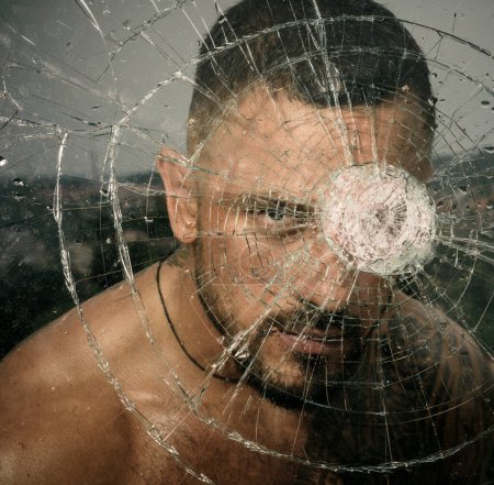 Photo for Macho man glasscutter behind crushed glass. Sexy hispanic tattooed man behind broken glass. Bullet hole in glass. Destruction and crush test concept. Man style - Royalty Free Image