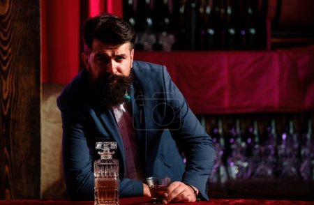 Téléchargez les photos : Concept de boisson de luxe Barman. L'homme à la barbe tient un verre avec de l'alcool au bar. Serveur barman en gilet vintage avec whisky ou scotch sur plateau - en image libre de droit