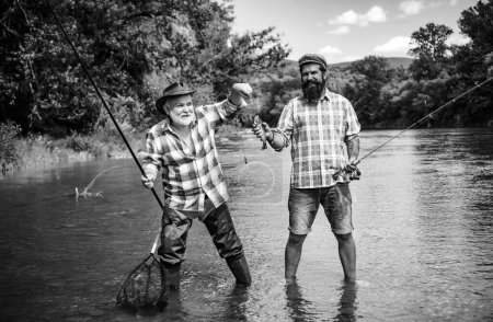 Téléchargez les photos : Des amis. Deux hommes amis pêche. Pêcheur à la ligne fait coulée, debout dans l'eau de la rivière. Vieux et jeune pêcheur - en image libre de droit